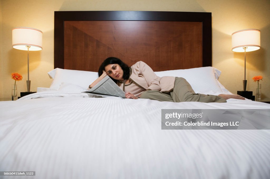 Mid adult woman lying on a bed and reading a newspaper