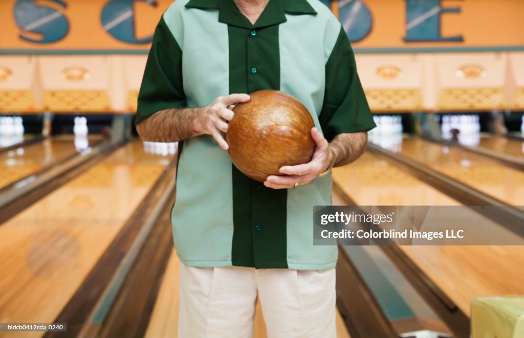 Mid section view of a mid adult man holding a bowling ball in a bowling alley