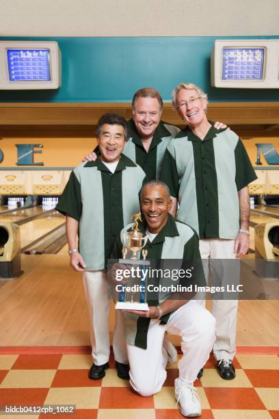 portrait of four mature men with a trophy in a bowling alley - bowling for buddies stock pictures, royalty-free photos & images