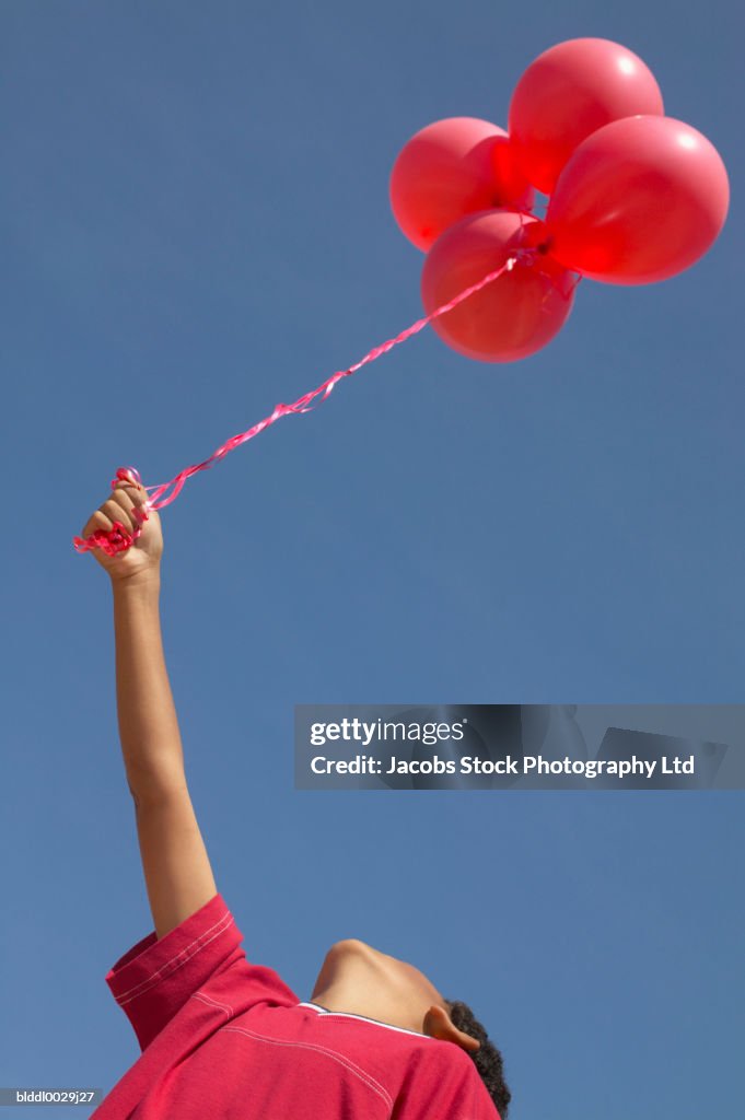 Low angle view of a young boy holding a bunch of balloons