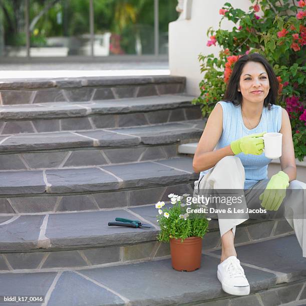 mid adult woman sitting on stairs and holding a cup of tea - dave and les jacobs stock-fotos und bilder
