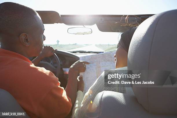 rear view of a mid adult couple in a convertible car and looking at a road map - dave and les jacobs stock-fotos und bilder