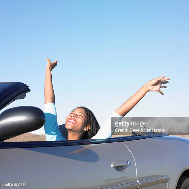 mid adult woman sitting in a convertible car and raising her hands - dave and les jacobs stock-fotos und bilder