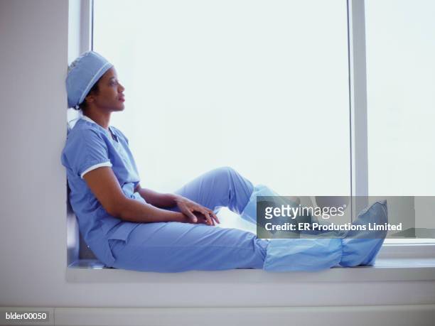 female surgeon sitting on a window ledge - er stock-fotos und bilder