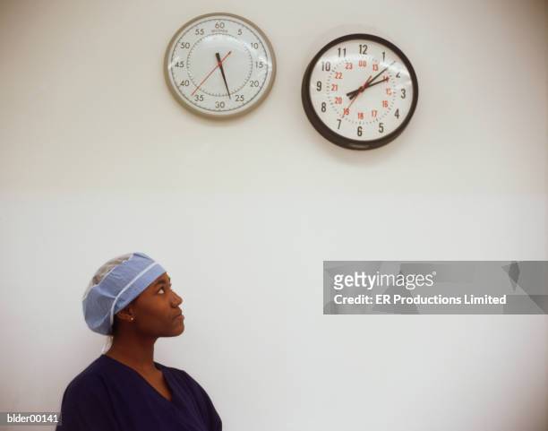 female nurse looking at a clock on a wall - erbore stock pictures, royalty-free photos & images