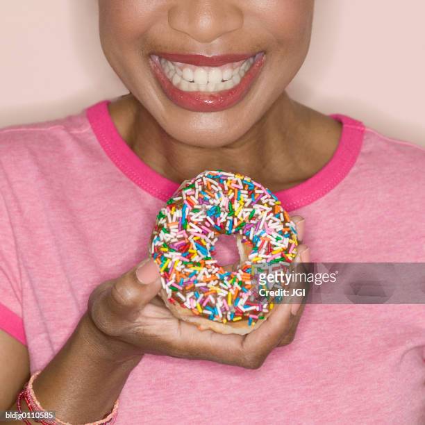 woman holding a doughnut smiling - eating donuts foto e immagini stock