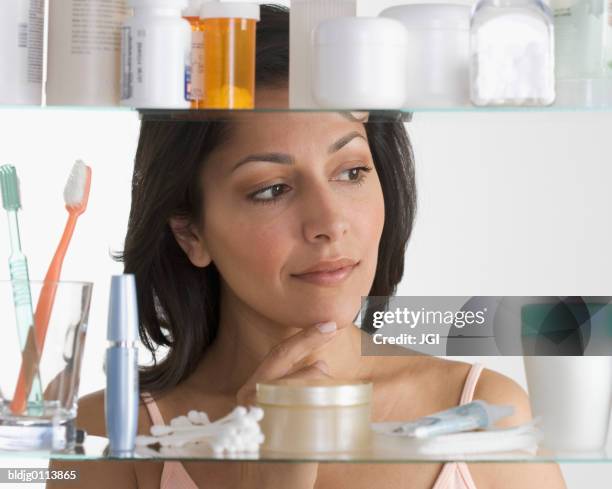 close-up of a mid adult woman standing in front of a bathroom cabinet - medicine cabinet stock pictures, royalty-free photos & images