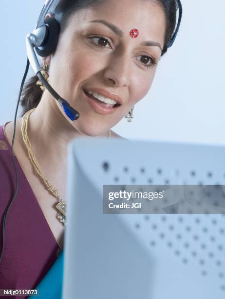 close-up of a mid adult woman wearing headset in front of a computer - traditional clothing stock pictures, royalty-free photos & images