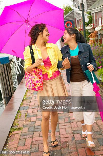 two young women walking under an umbrella talking - under the skirt stock-fotos und bilder