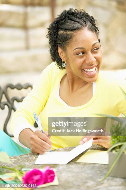 young woman sitting at a table writing in a greeting card - card table stock pictures, royalty-free photos & images