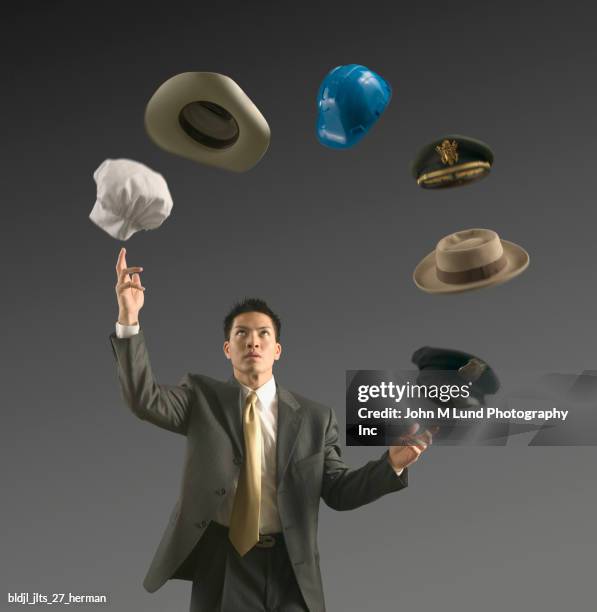 young businessman juggling assorted hats - juggling act stock pictures, royalty-free photos & images