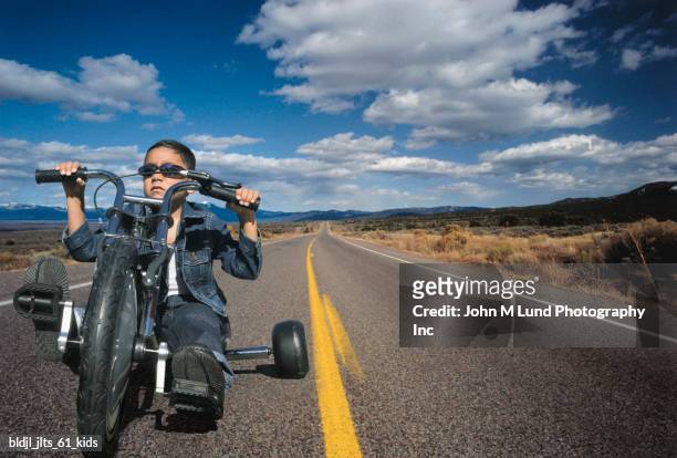 portrait of a young boy riding a toy motorcycle on a highway - john lund ストックフォトと画像