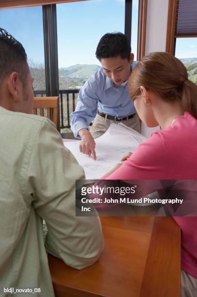 architect with a young couple looking over blueprints - john lund stock-fotos und bilder