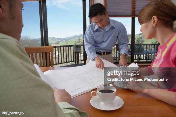 architect with a young couple looking over blueprints - john lund ストックフォトと画像