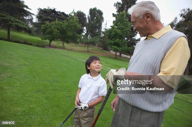 young boy standing with am senior man at a golf course - golf short iron stock pictures, royalty-free photos & images