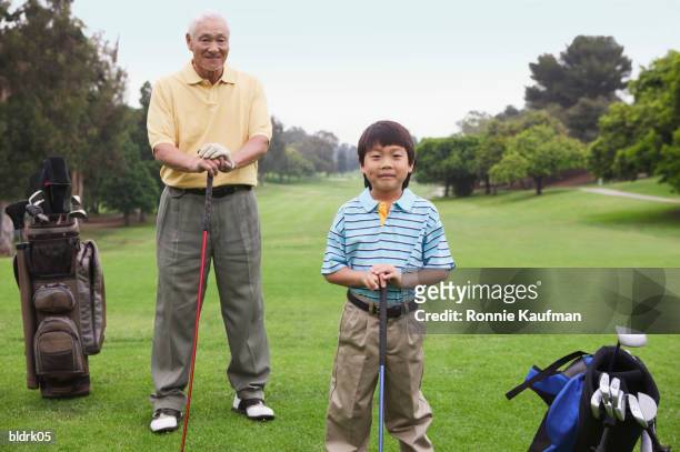 portrait of a young boy and senior man standing together holding golf clubs - golf short iron stock pictures, royalty-free photos & images