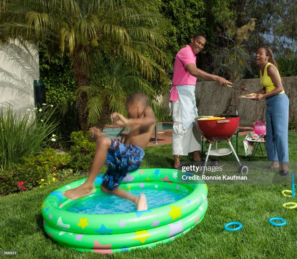 Family having a barbeque on a lawn with a young boy jumping into a pool