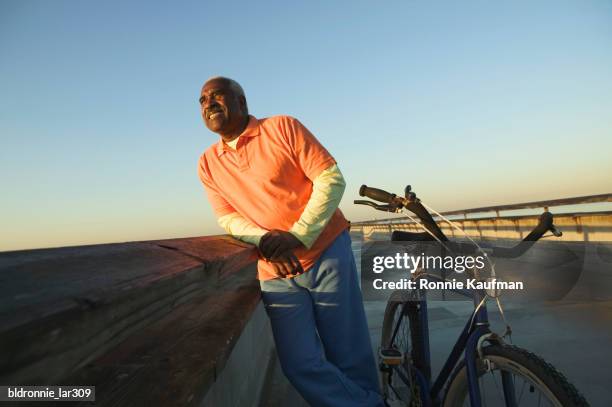 mature man leaning against railing on a bridge - ronnie kaufman stockfoto's en -beelden