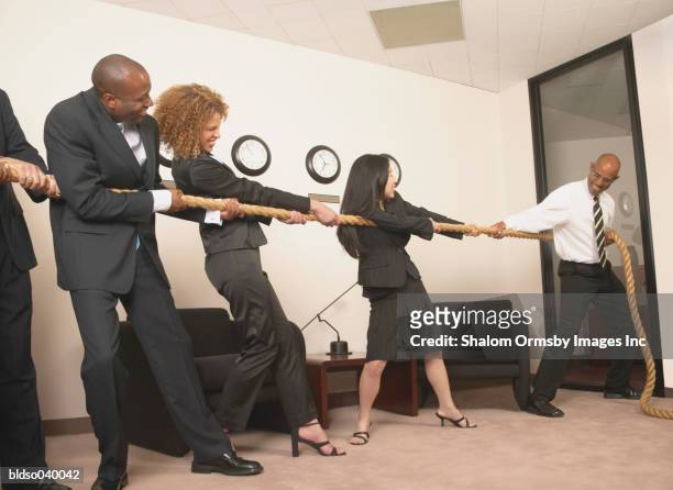 group of business executives playing tug of war in the office - war stock-fotos und bilder