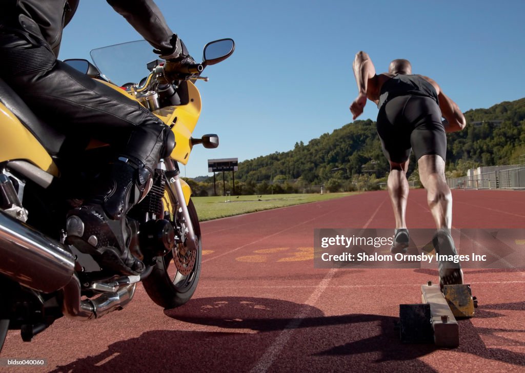 Rear view of a young man at the starting position on a running track along side a motorcycle