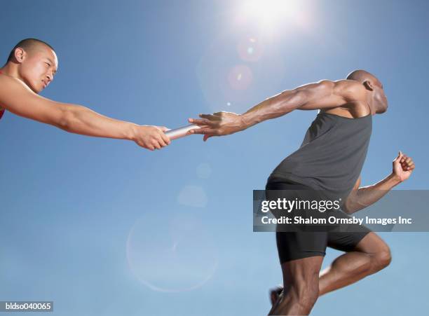low angle view of one man passing a baton to another in a relay race - course sur piste hommes photos et images de collection