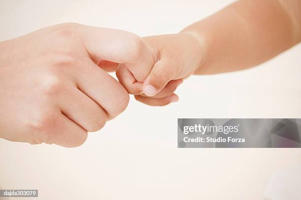 a baby girl holding her mother's finger - forza fotografías e imágenes de stock