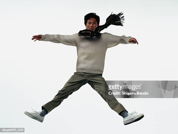 young asian man in pants & sweat-shirt and scarf, jumping in mid-air - legs apart imagens e fotografias de stock
