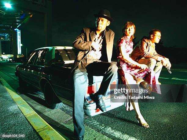 two men and a woman sitting on car - woman capturing city night stockfoto's en -beelden