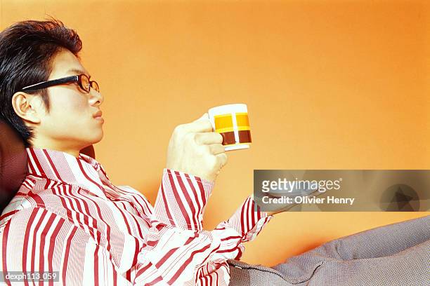 young man relaxing on couch, holding saucer and cup - henry stockfoto's en -beelden