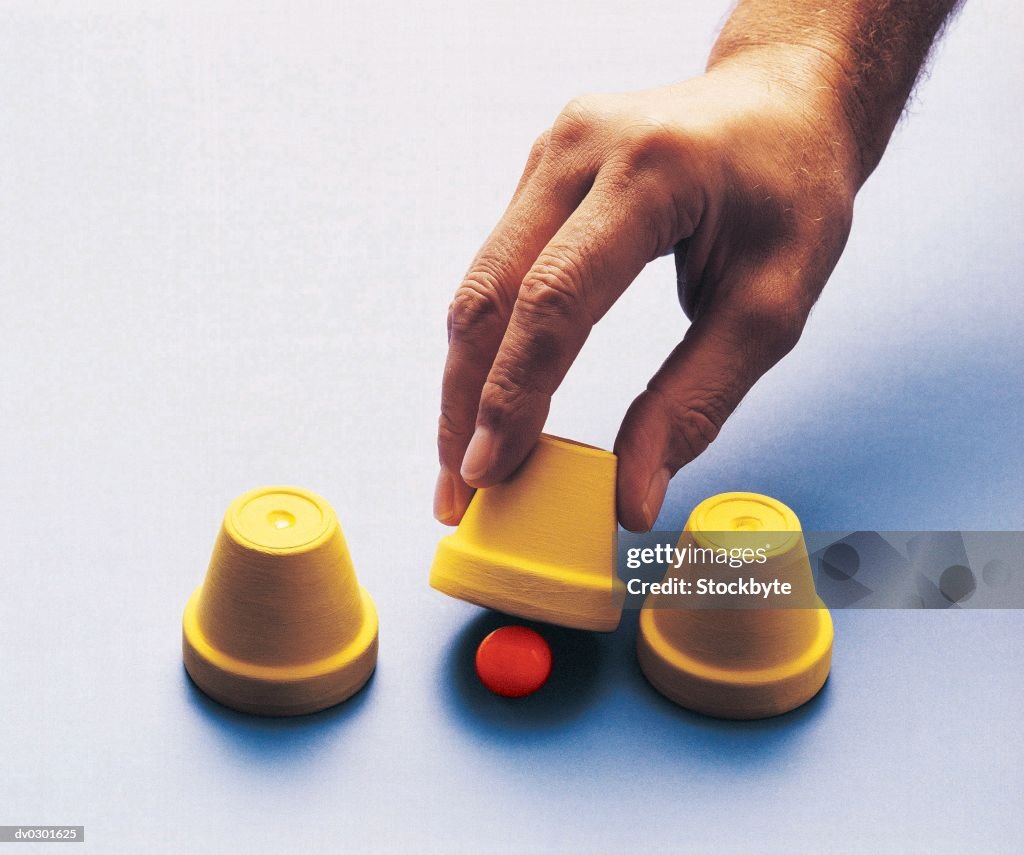 Hand lifting up small pot to reveal red ball