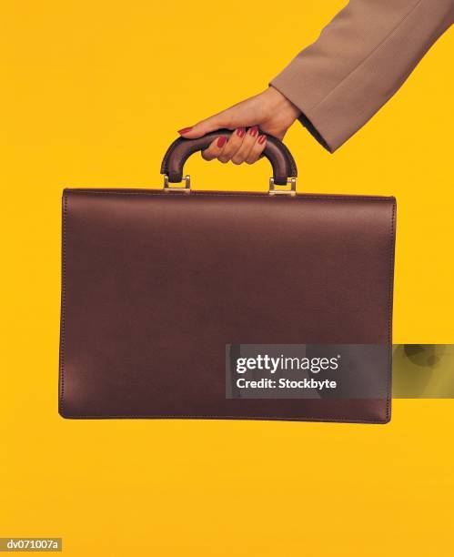 businesswomans hand holding brown briefcase, yellow background - briefcase stock pictures, royalty-free photos & images