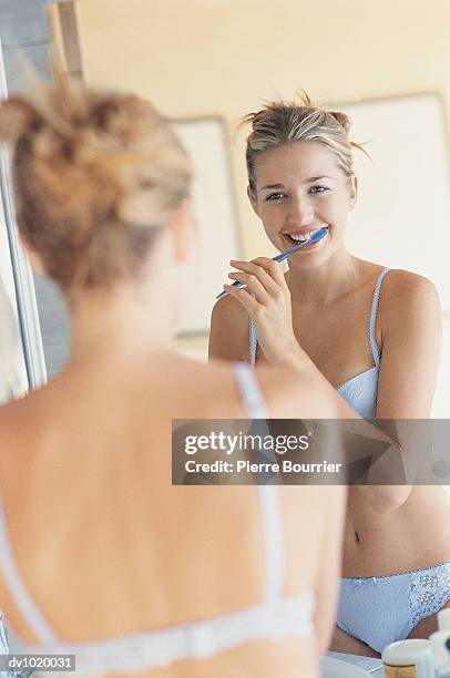 young woman in her bra and knickers brushing her teeth and looking in the bathroom mirror - knickers photos fotografías e imágenes de stock