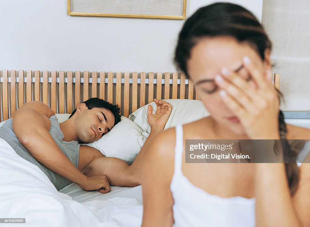 Woman Sitting on a Bed in a Bedroom, Man Sleeping