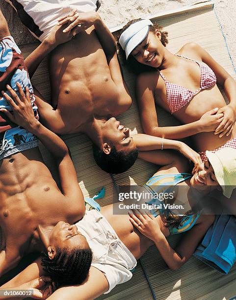 four teenagers lying on a beach - sunbathing stock pictures, royalty-free photos & images