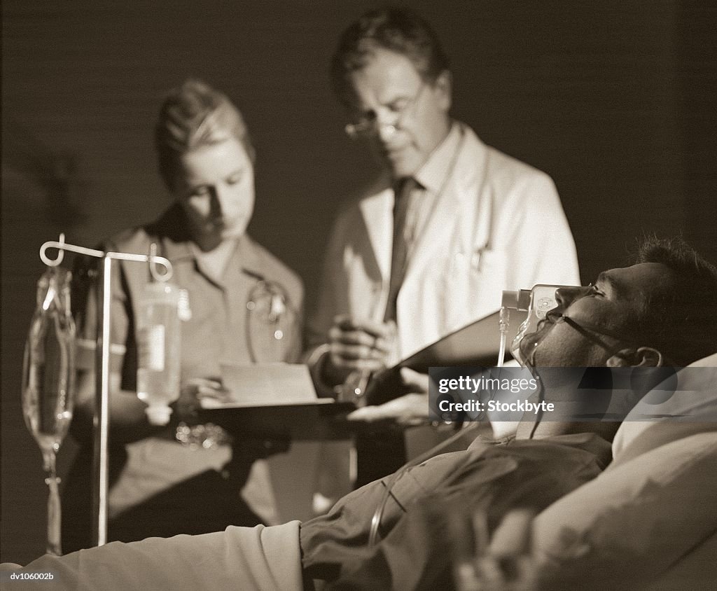 Man lying in hospital bed, wearing oxygen mask; doctors in background