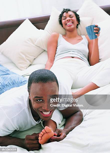 couple lying on a bed, man tickling woman's foot - woman lying on stomach with feet up fotografías e imágenes de stock