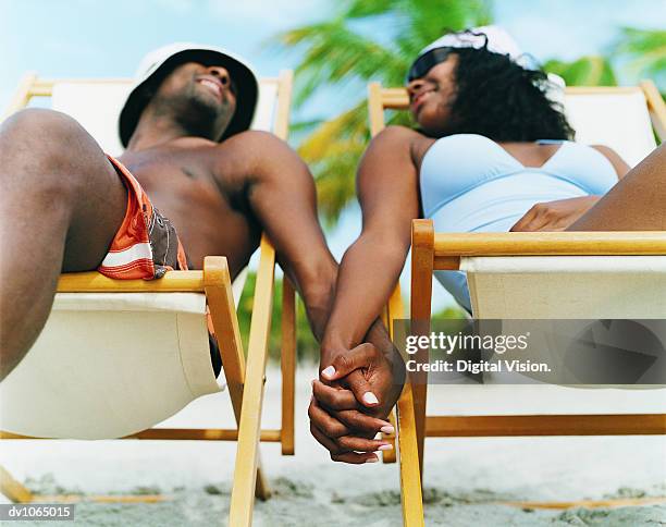 couple sitting on deck chairs, holding hands on the beach - romantic fotografías e imágenes de stock