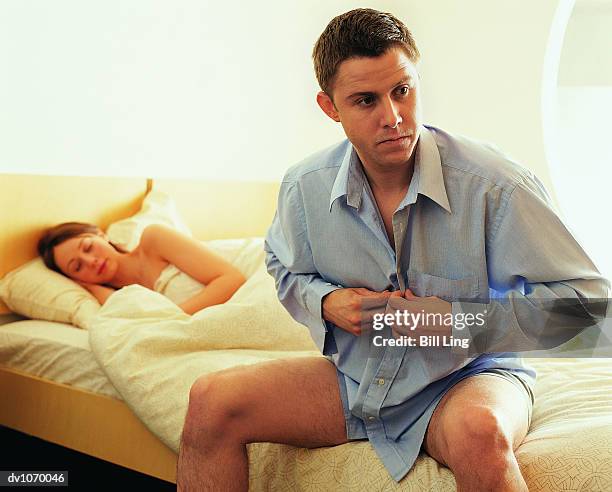 man getting dressed on the bed, whilst a woman sleeps - early termination bildbanksfoton och bilder