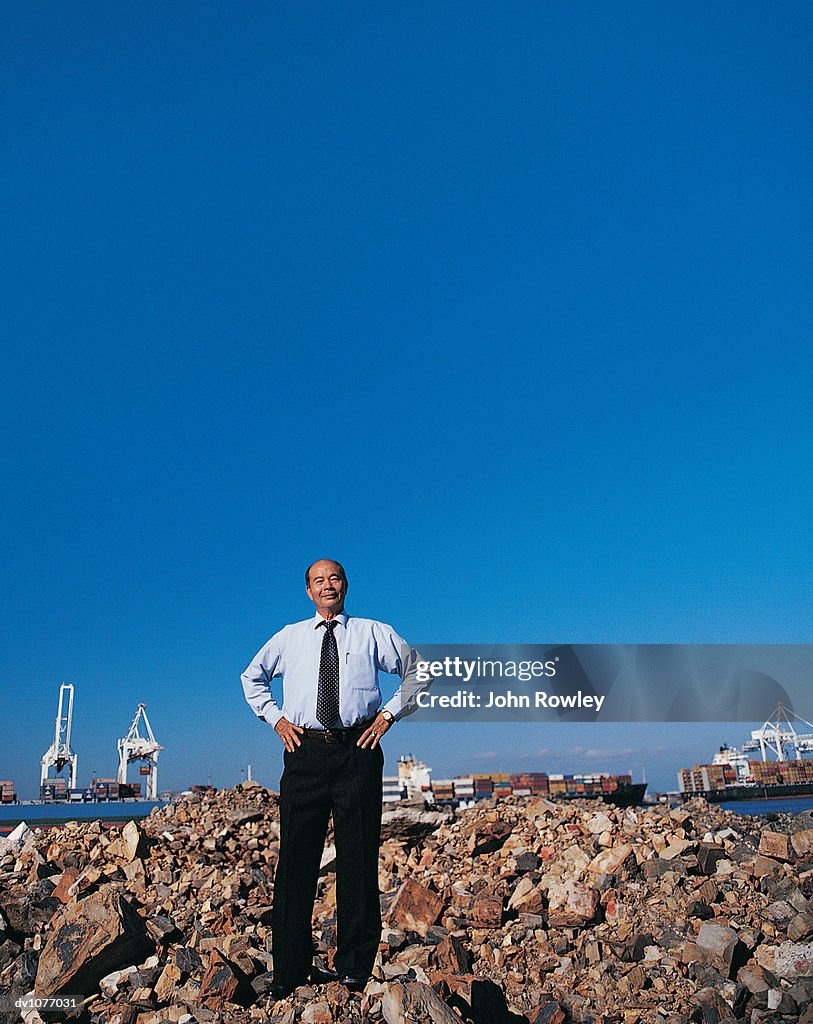 Portrait of a Mature Businessman Standing on a Pile of Rubble With His Hands on His Hips in a Harbour