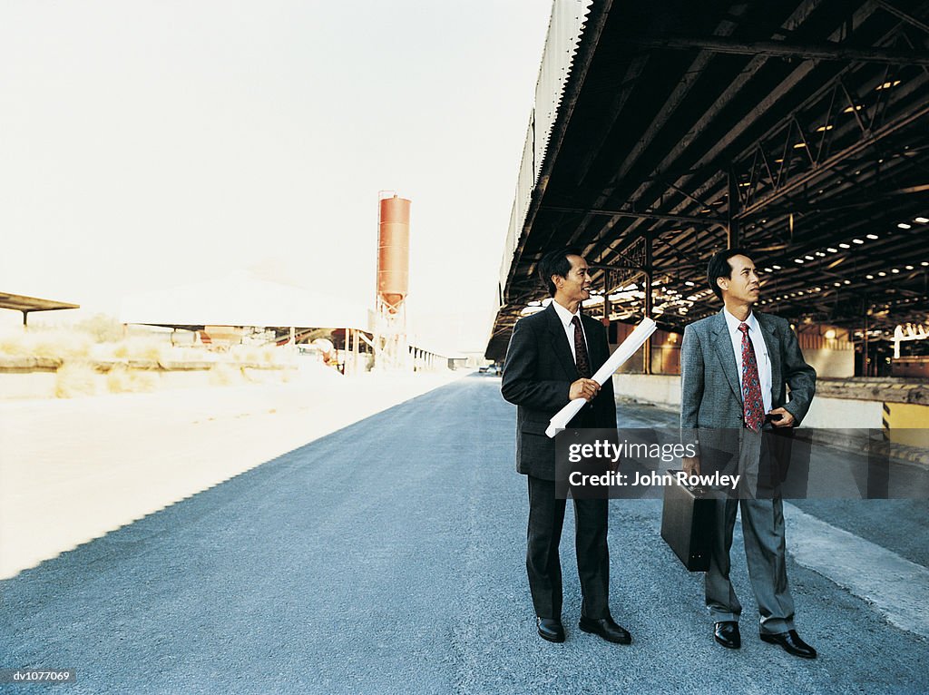 Two Businessmen Standing in an Industrial Park Looking at a Factory Building