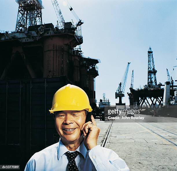mature businessman wearing a hard hat using a mobile phone in a harbour - mobile crane - fotografias e filmes do acervo
