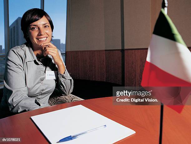 portrait of a businesswoman sitting with her hand on her chin at a table with an italian flag in a conference room - key speakers at the international economic forum of the americas conference of montreal stockfoto's en -beelden