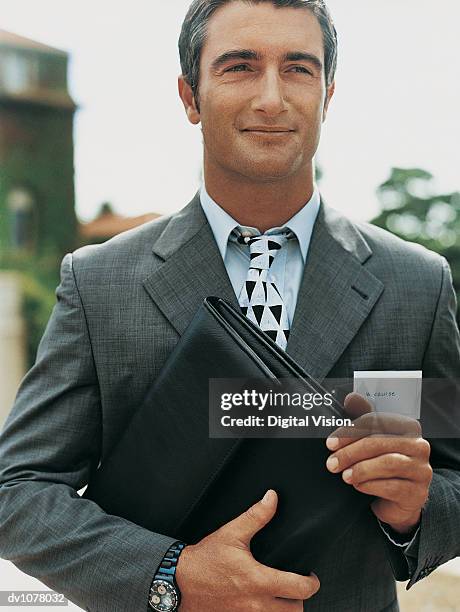 portrait of a satisfied businessman holding a folder and wearing an id card - ojos grises fotografías e imágenes de stock