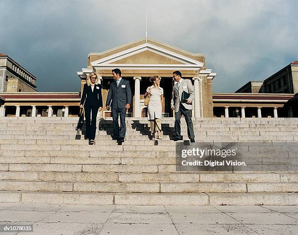 four business executives walking down stone steps in front of a building - look down stock-fotos und bilder