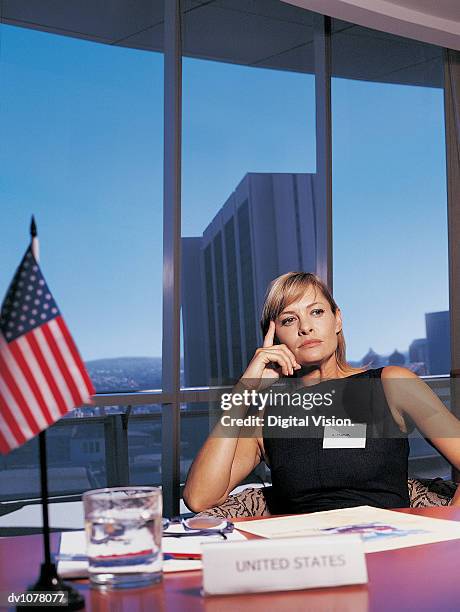 portrait of a businesswoman sitting at a conference table by the stars and stripes with her hand on her chin - upper midtown manhattan stock pictures, royalty-free photos & images