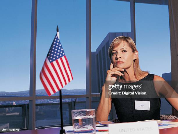 portrait of a businesswoman sitting at a conference table by the stars and stripes with her hand on her chin - upper midtown manhattan stock pictures, royalty-free photos & images