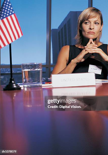 portrait of a businesswoman sitting at a conference table by the stars and stripes with her hand on her chin - upper midtown manhattan bildbanksfoton och bilder