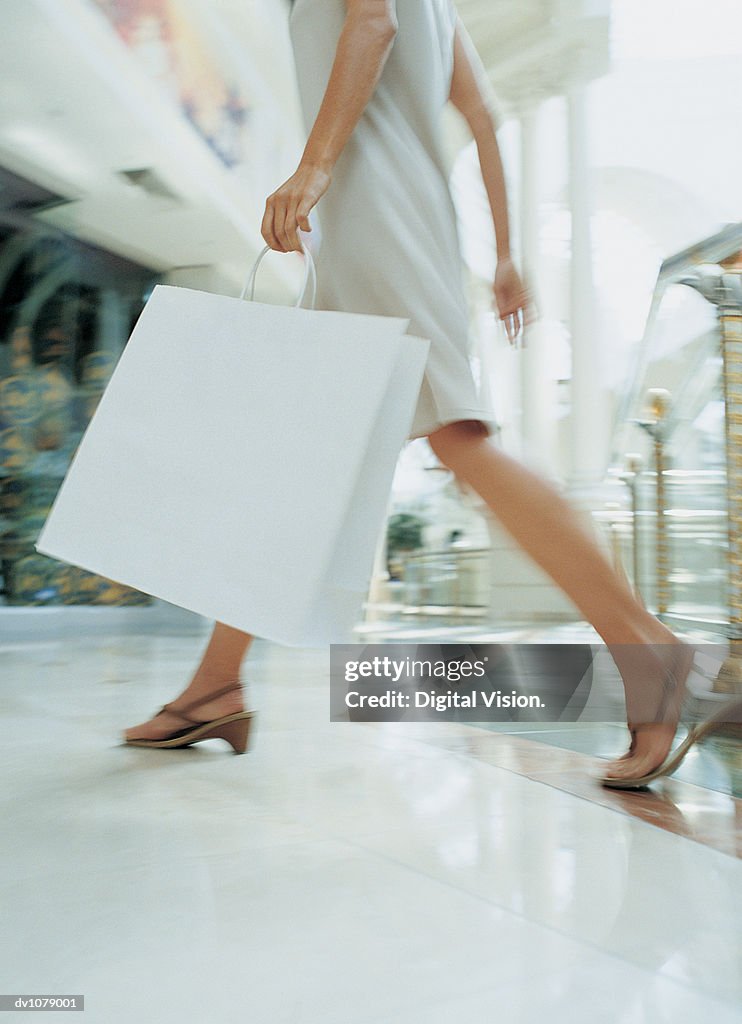 Close up of a the Legs of a Woman Walking Through a Shopping Mall Carrying a Shopping Bag
