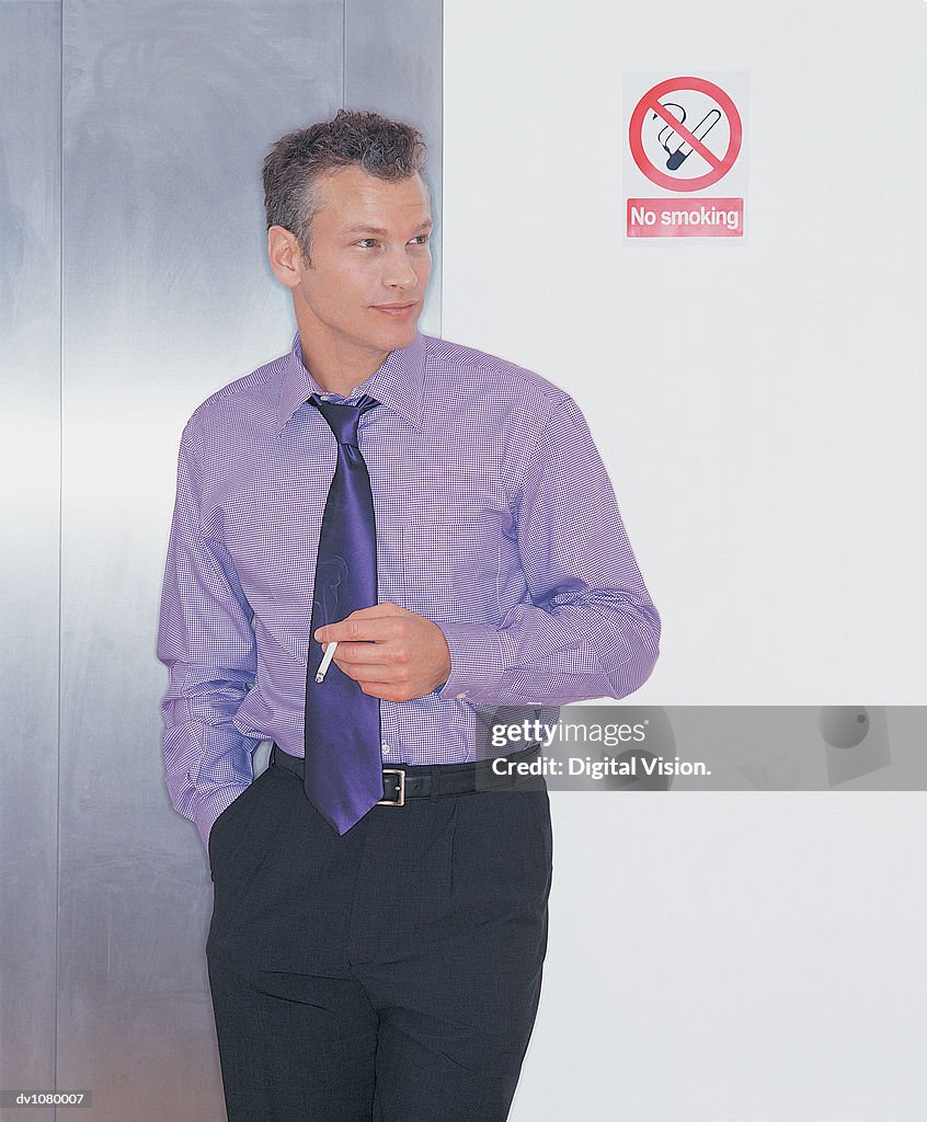 Young Businessman Smoking a Cigarette Next to a No Smoking Sign