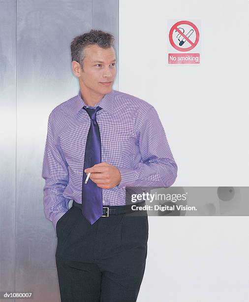 young businessman smoking a cigarette next to a no smoking sign - anti smoking bildbanksfoton och bilder